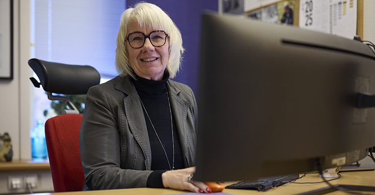 Kvinna sitter vid en datorskärm och håller i en mobiltelefon