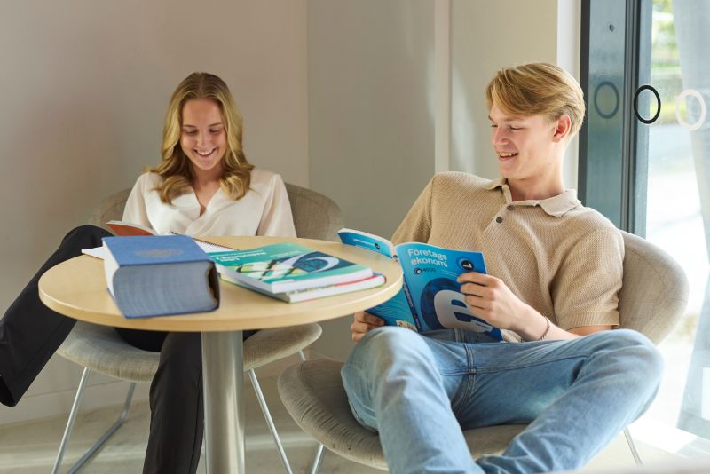 Två elever i klassrum som håller i kurslitteratur.