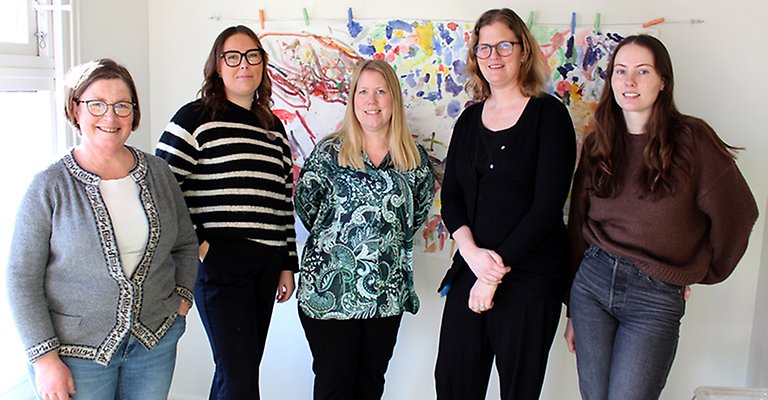 Fem kvinnor står bredvid varandra. I bakgrunden finns en färgglad tavla från Ugglans konst